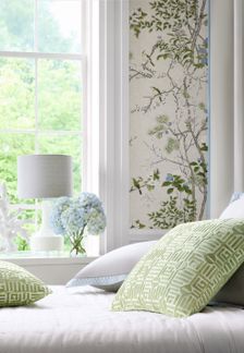 a white bed with green and blue pillows in front of a wallpapered window