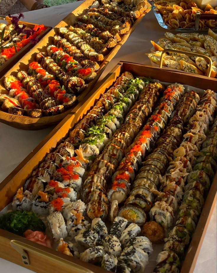 an assortment of food is displayed in trays on the table, including sushi and rolls