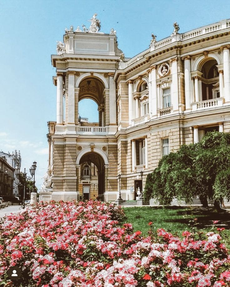 a large building with many flowers in the front and on the ground next to it