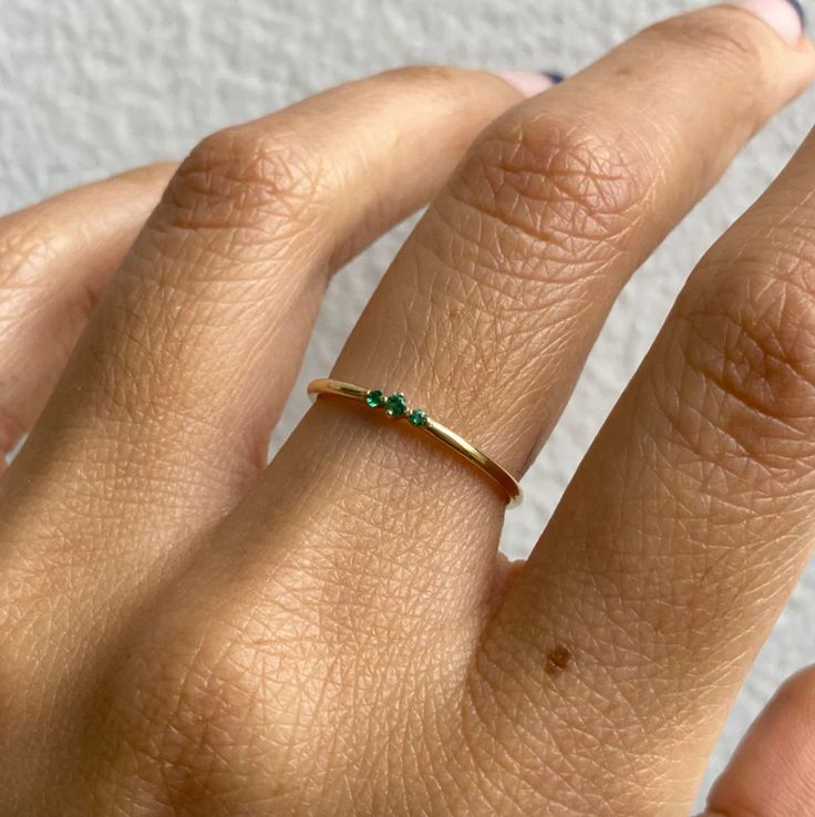 a woman's hand with a gold ring and green stones on it, against a white background