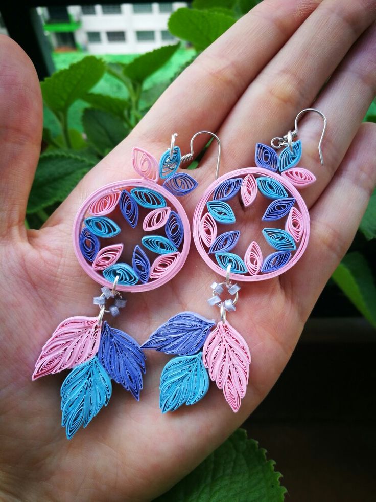 a pair of earrings made out of paper with leaves and beads hanging from the ends