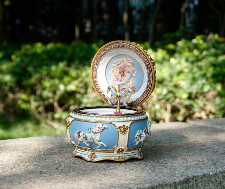 an ornate blue and white box sitting on top of a stone wall next to trees