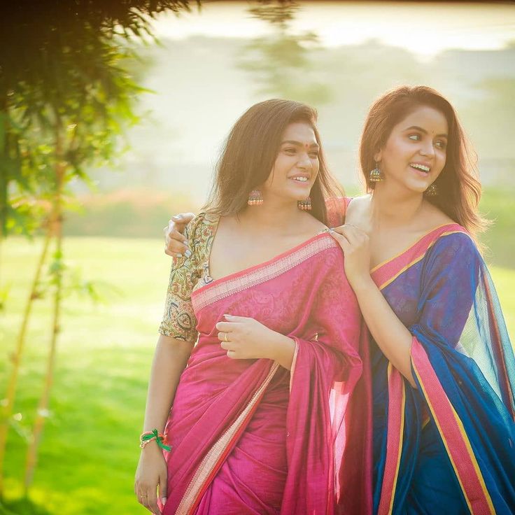 two beautiful women in sari standing next to each other on the green grass field