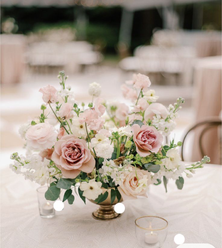 a vase filled with lots of flowers on top of a white tablecloth covered table