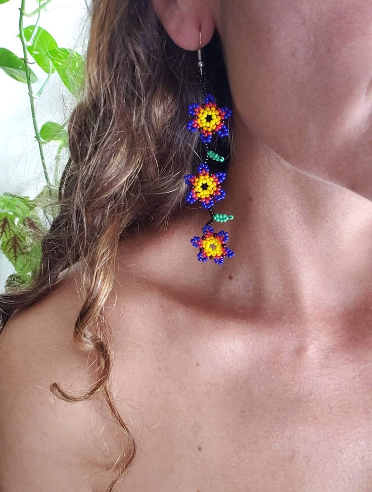 Welcome Spring whit these beautiful Multicolor Daisies creeper flowers earrings, made by Huichol Hands in Mexico. The Huichol art is a form of writing, as through the creations, the Huichol tell us their stories and myths. In each Huichol crafts leave a piece of your life. Handmade Multicolor Flower Earrings, Multicolor Handmade Flower Earrings, Multicolor Flower-shaped Earrings With Dangling Beads, Yellow Flower Earrings With Colorful Beads, Bohemian Blue Jewelry With Handmade Flowers, Flower Shaped Dangling Beads Earrings For Festivals, Flower-shaped Festival Earrings With Dangling Beads, Flower Shaped Festival Earrings With Dangling Beads, Multicolor Flower Earrings For Festival