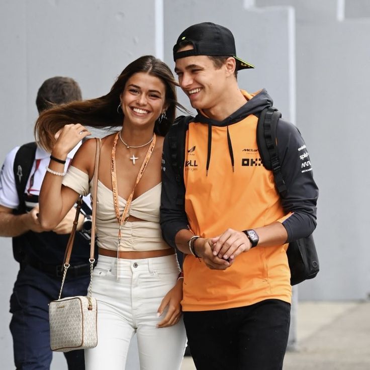 a man and woman are walking down the street together, one is wearing an orange vest