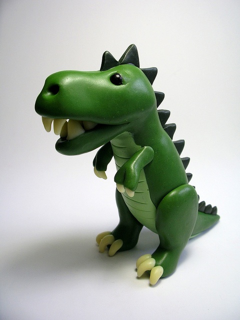 a green toy dinosaur with its mouth open and teeth wide open, on a white background