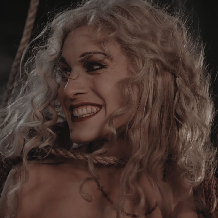 a close up of a person with long blonde hair and tattoos on her chest, smiling at the camera