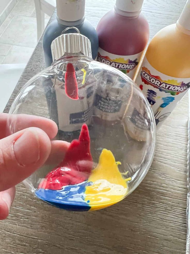 a hand is holding a small glass ornament with paint and glue on it