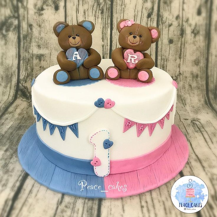 two teddy bears sitting on top of a cake with pink, blue and white frosting