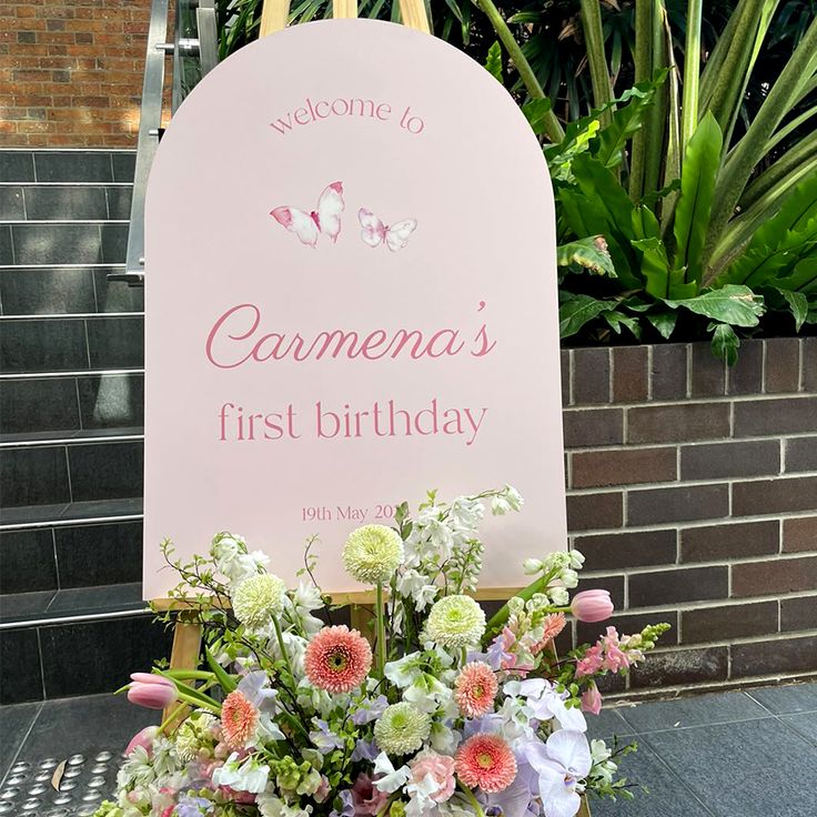 a pink sign that says welcome to someone's first birthday with flowers in it