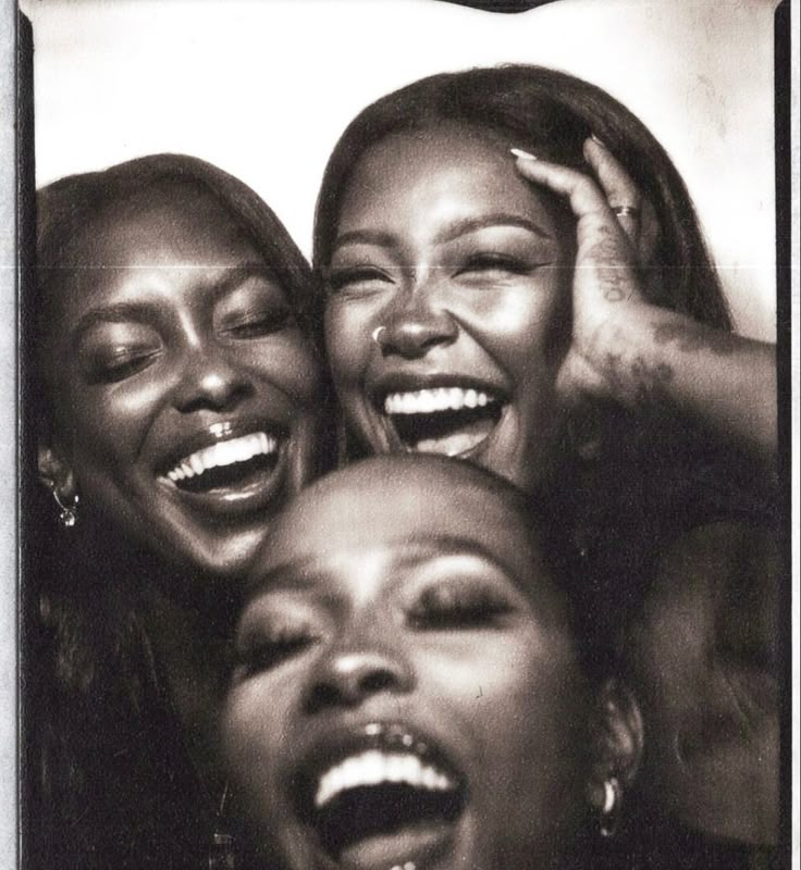 three women laughing together with their mouths open and one holding her head in the other's hands