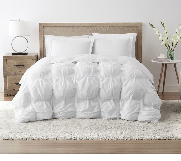 a bed with white comforter and pillows on top of it in a room next to a night stand