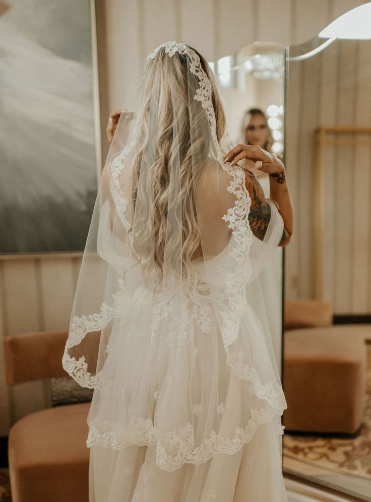 the back of a bride's dress as she stands in front of a mirror