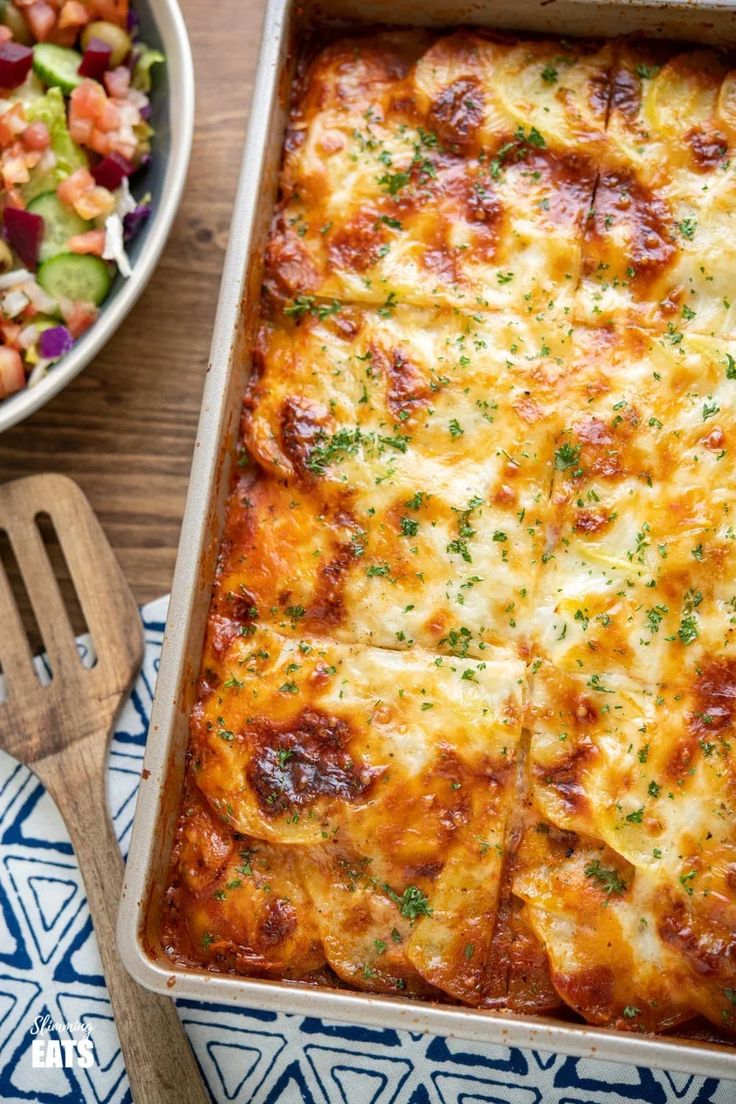 a casserole dish with meat and vegetables in it next to a bowl of salad