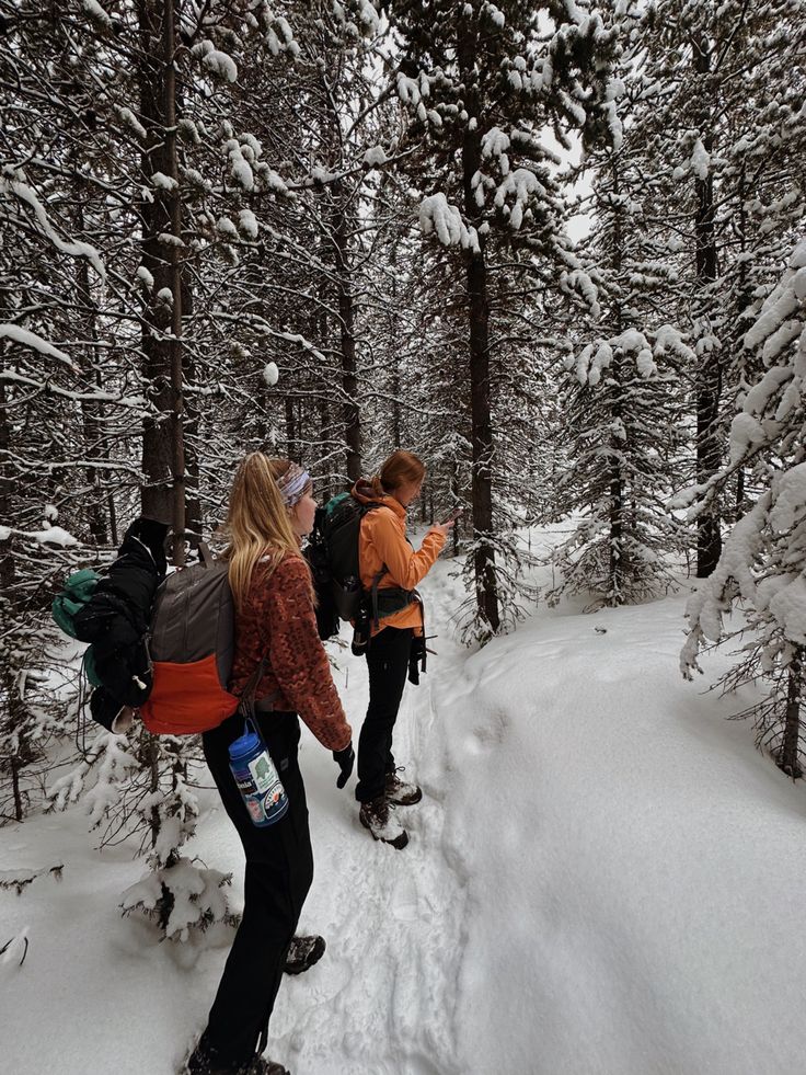 two people are walking through the snow in skis and backpacks on a trail