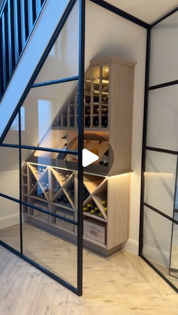 a room that has some wine bottles in the glass shelves on the wall and stairs to the second floor