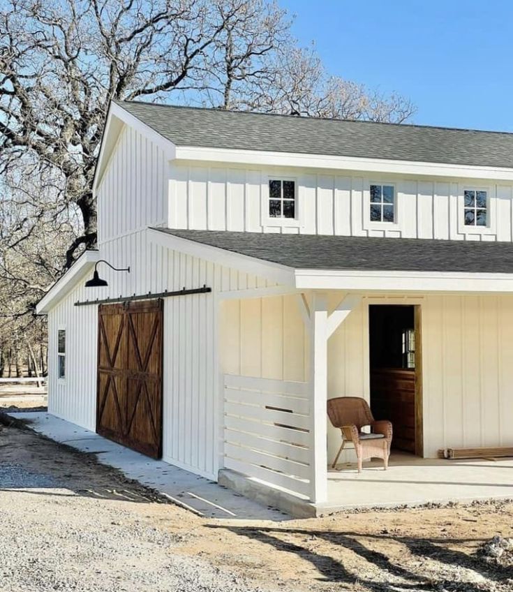 a white barn with a brown chair in the front door and windows on the side