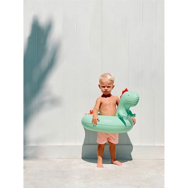 a toddler standing in an inflatable pool with a toy dinosaur on it