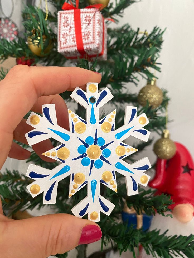 a hand holding a snowflake ornament in front of a christmas tree