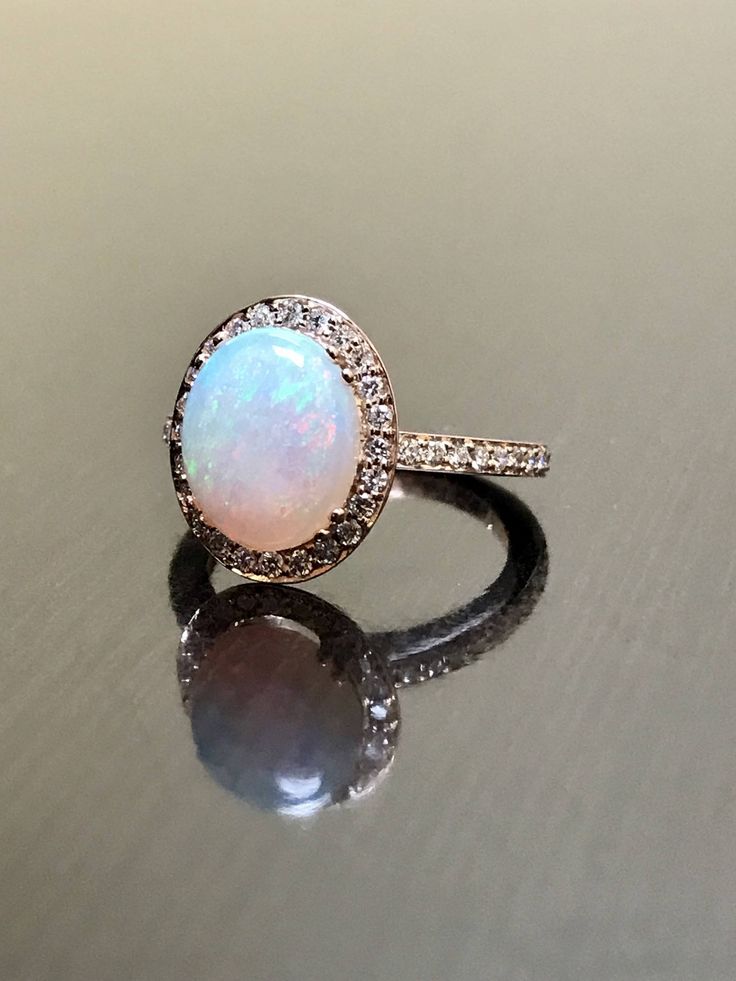 DeKara Designs Collection Our latest design! An elegant and lustrous Opal cabochon surrounded by beautiful diamonds in a halo setting. Metal- 14K Rose Gold, .583. Size- 4-12 Stones- Center Features a Oval Fiery Opal Cabochon Cut 2.60-2.90 Carats, 11.10 MM Long, 9 MM Wide, 44 Round Diamonds, F Color VVS Clarity, 0.35 Carats. Latest of my creations. A beautiful Opal Halo Diamond Ring. The Opal is professionally prong set in between 4 double prongs. There are 10 pave set round diamonds on each side Elegant White Gold Diamond Ring With Cabochon, Round Cabochon Diamond Ring, Exquisite Rose Gold Rings With Accent Stones, Luxury Rose Gold Round Wedding Ring, Luxury Diamond Opal Ring, Luxury Rose Gold Opal Gemstone Ring, Anniversary Diamond Cabochon Ring, Rose Gold Halo Ring With Diamond Accents, Rose Gold Halo Setting Round Wedding Ring