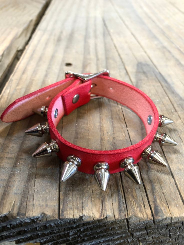 a red leather collar with spiked spikes on the front and back of it, sitting on a wooden surface