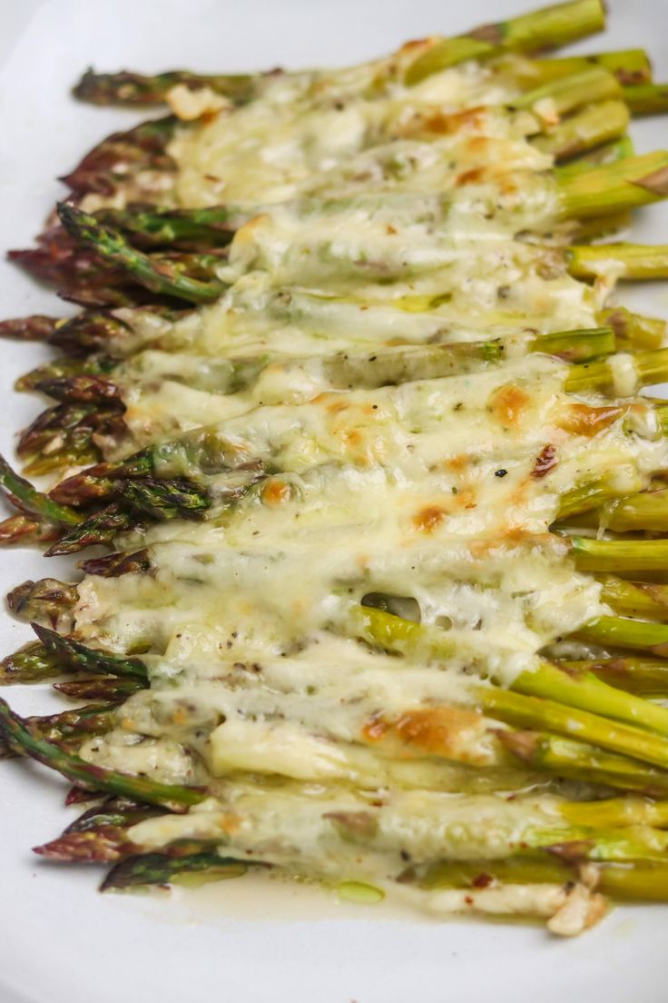 asparagus covered in melted cheese on a white plate