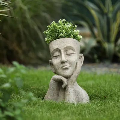 a statue with a planter on its head in the grass