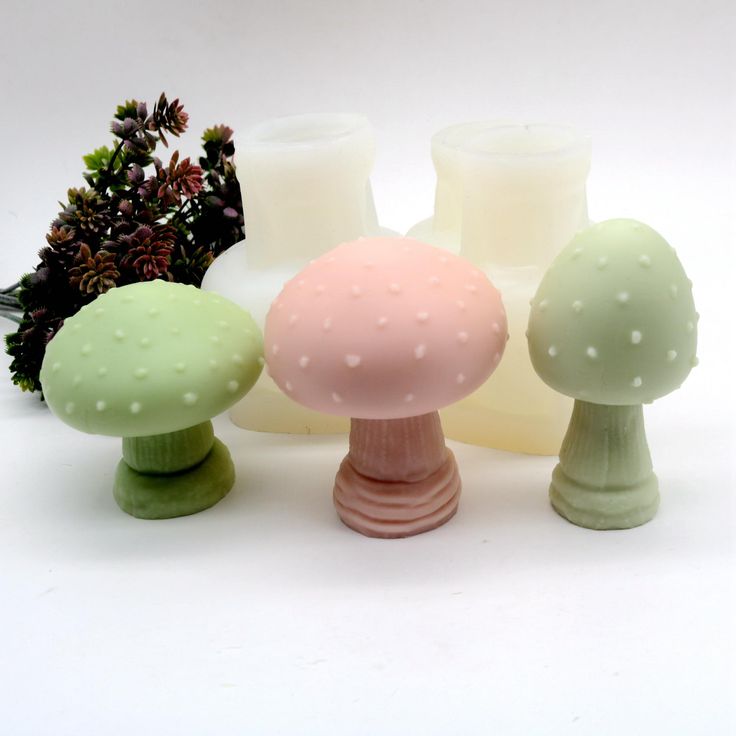 three different colored candles sitting next to each other on a white surface with plants in the background