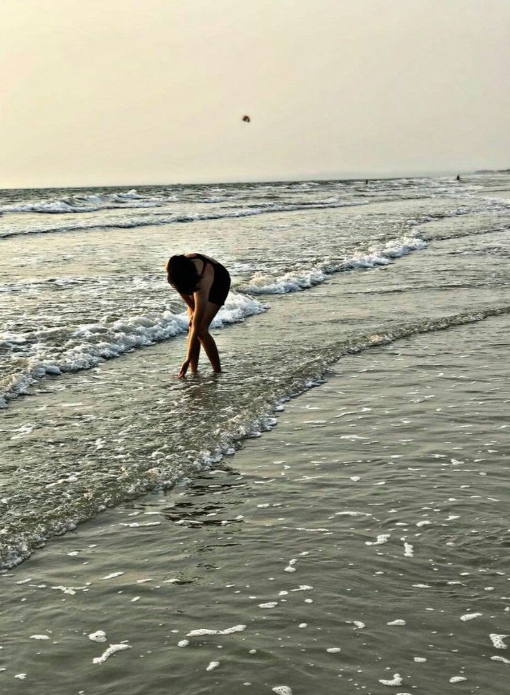 a person bending over in the water at the beach