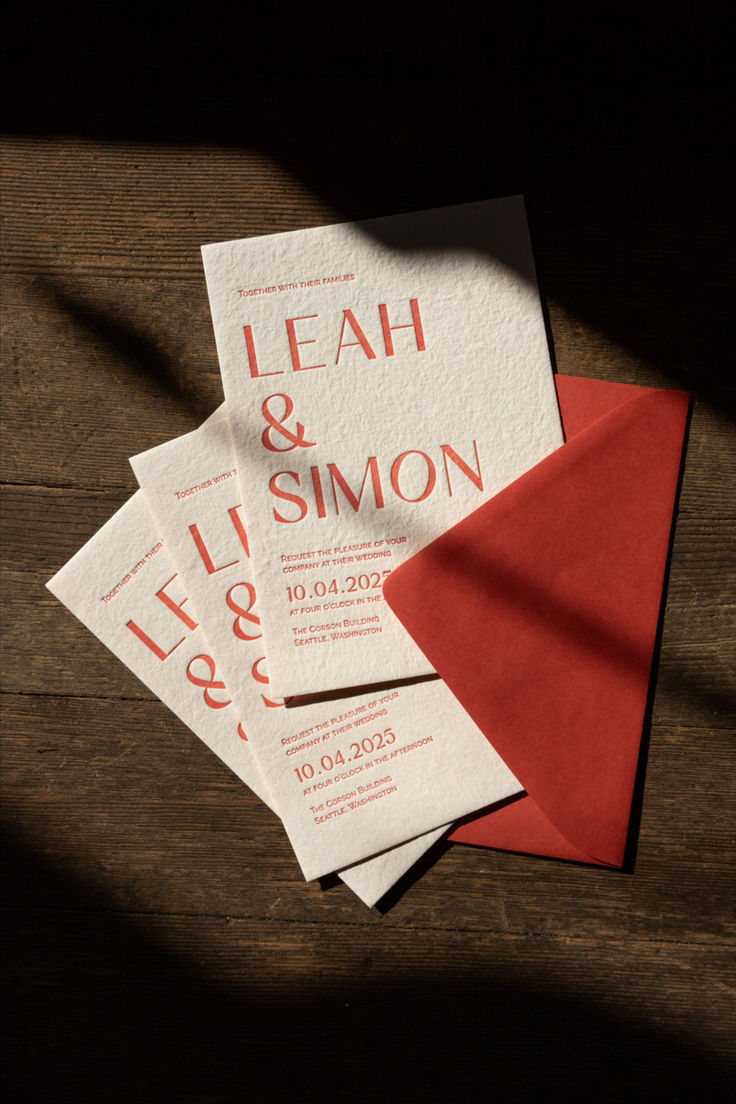 wedding stationery with red envelopes and letterpress printed on them sitting on a wooden table