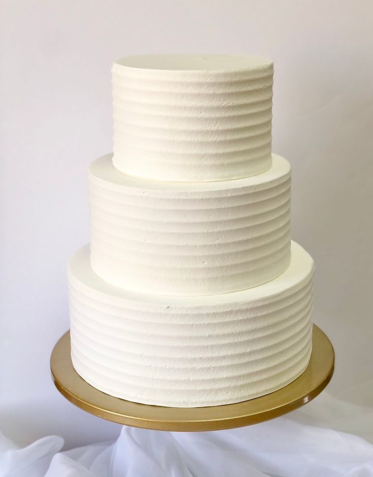 a three tiered white wedding cake on a gold platter