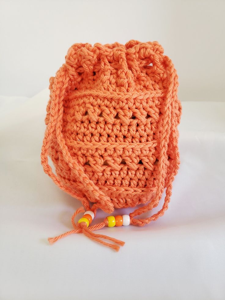 an orange crocheted bag with tassels and beads on the handle is sitting on a white surface