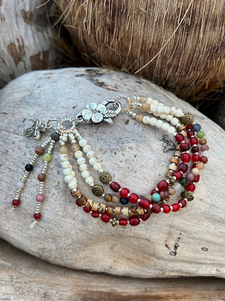 A touch of Africa, all the red beads are handmade in Africa in all sizes and shapes, gemstones right throughout and white howlite stones, brass evil eye beads, with jasper gemstones, attached with a silver flower clasp. 4 stands of beautiful colours.  7.8 inches long Red Spiritual Beaded Bracelets With Natural Stones, Spiritual Red Beaded Bracelets With Natural Stones, Red Bohemian Bracelet Beads, Red Bohemian Beaded Bracelets With Natural Stones, Hippie Style Red Jewelry For Gift, Bohemian Red Beaded Bracelets With Spacer Beads, Bohemian Red Beaded Bracelet With Spacer Beads, Red Multi-strand Beaded Bracelets, White Hippie Bracelet Jewelry