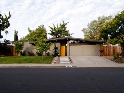 a house that is sitting on the side of a road with trees in front of it