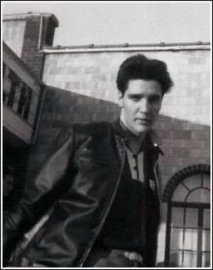 a black and white photo of a man in a leather jacket leaning against a wall