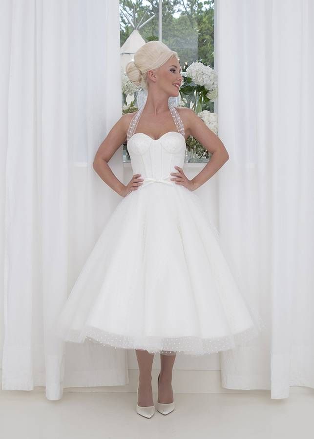 a woman standing in front of a window with her hands on her hips wearing a white dress