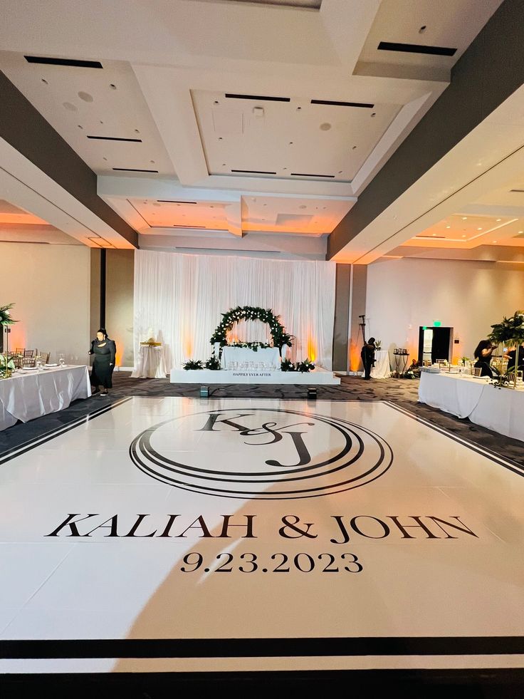 the reception room is decorated with white linens and black lettering on the dance floor