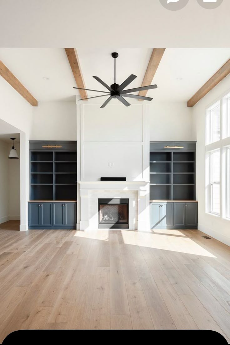 an empty living room with wood floors and ceiling fan in the center, surrounded by built - in bookshelves