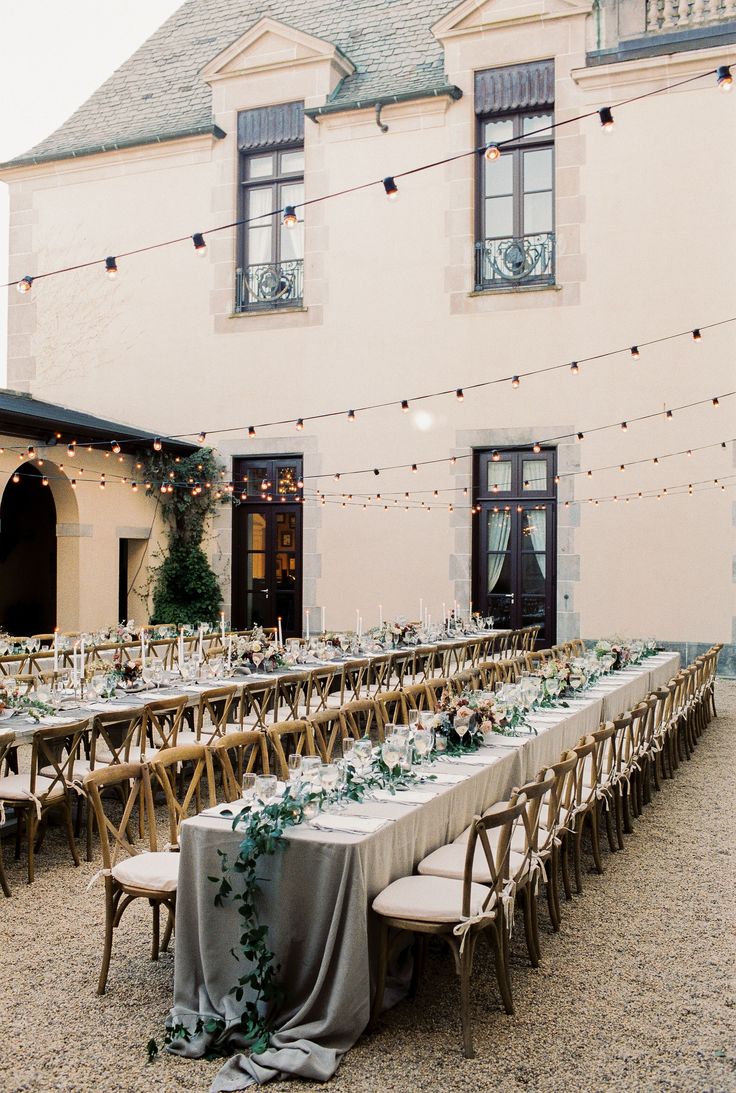 a long table set up for an outdoor wedding reception in front of a large building