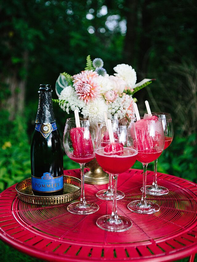 wine glasses and bottles are sitting on a red table with flowers in the vases