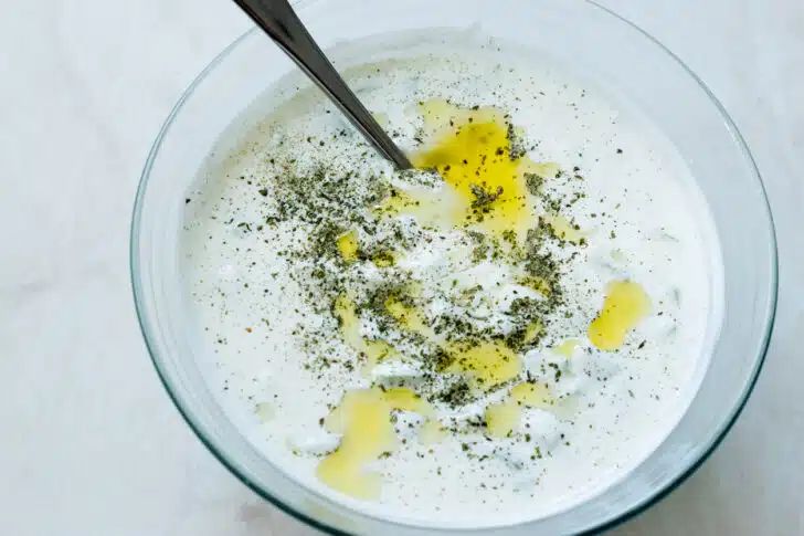 a glass bowl filled with food on top of a white countertop next to a wooden spoon