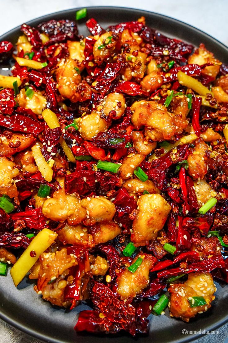 a black plate topped with chicken and veggies covered in sesame seed flakes