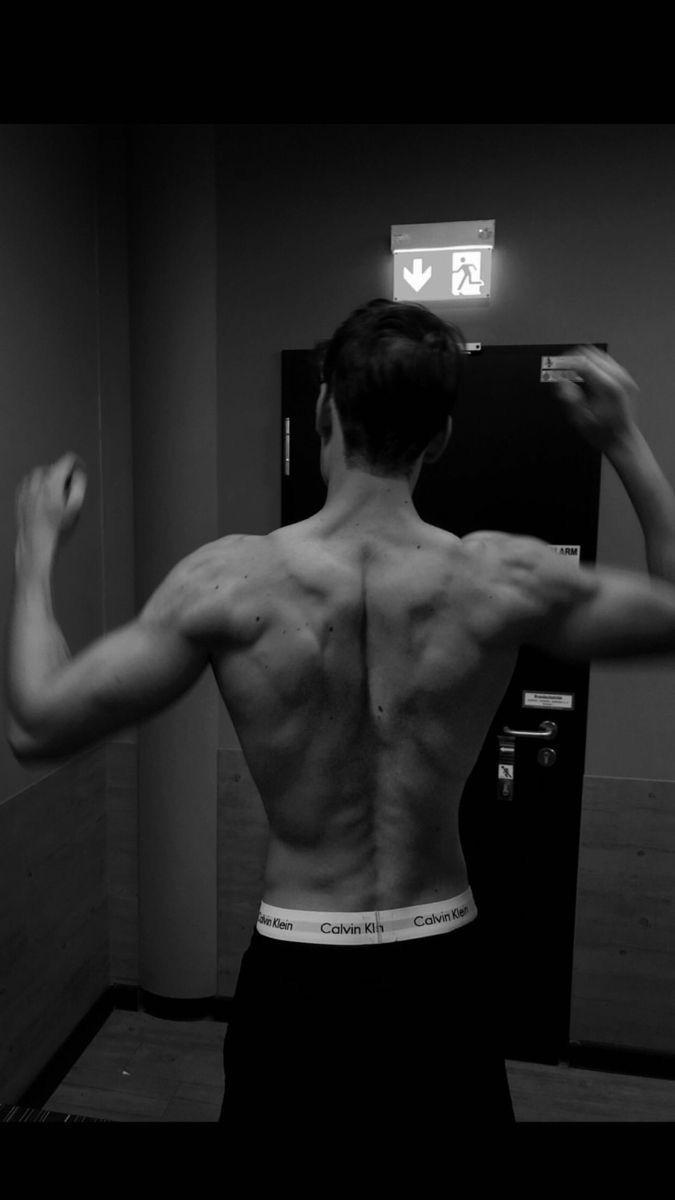 a man with his back turned to the camera in front of a mirror, showing his muscles