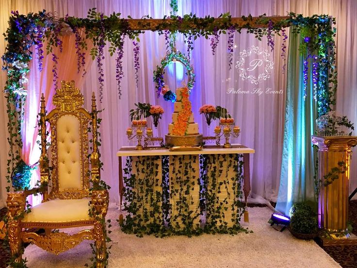 a decorated stage with flowers and greenery on the top, along with a gold chair