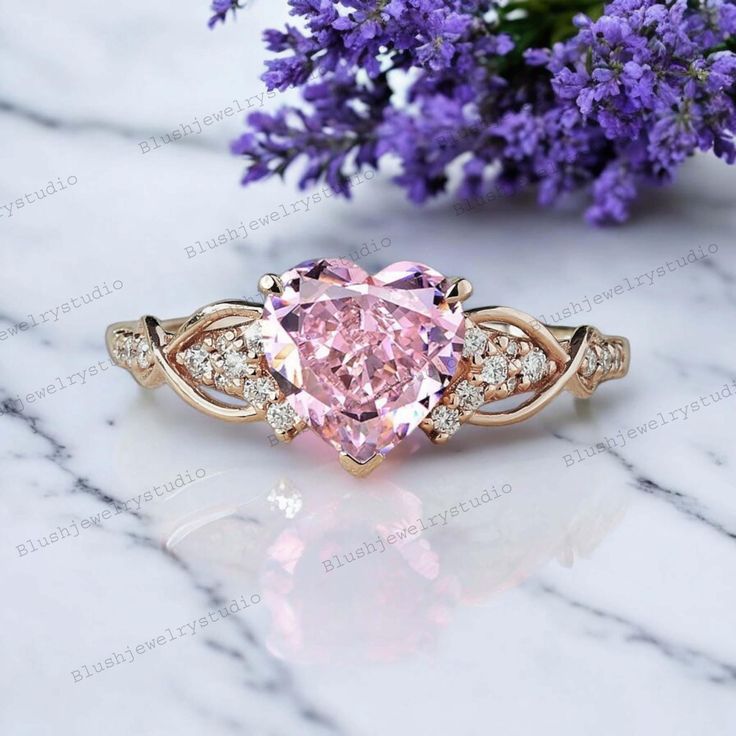 a pink diamond ring sitting on top of a white marble table next to purple flowers