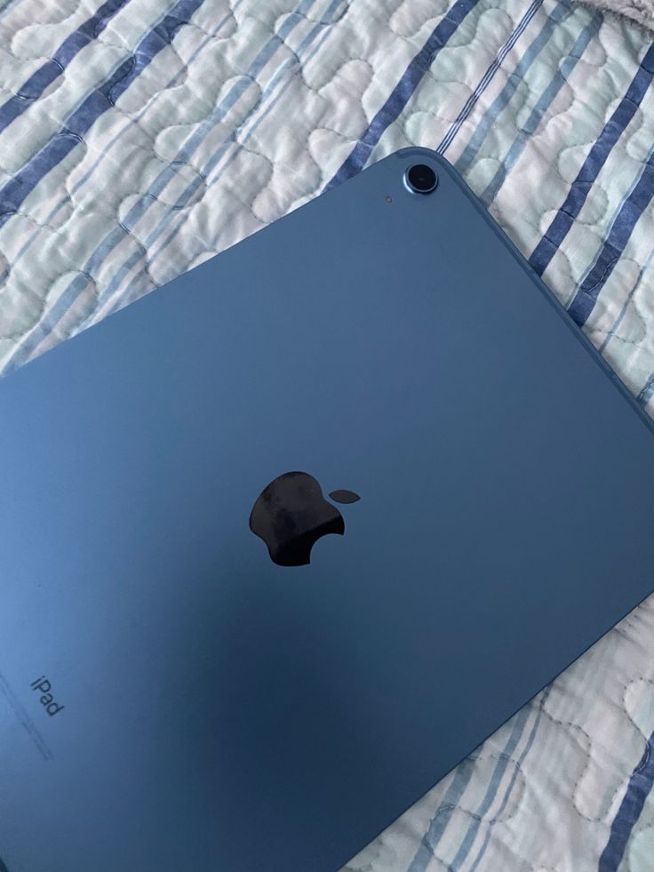 an apple ipad is sitting on a bed with a blue and white striped blanket behind it