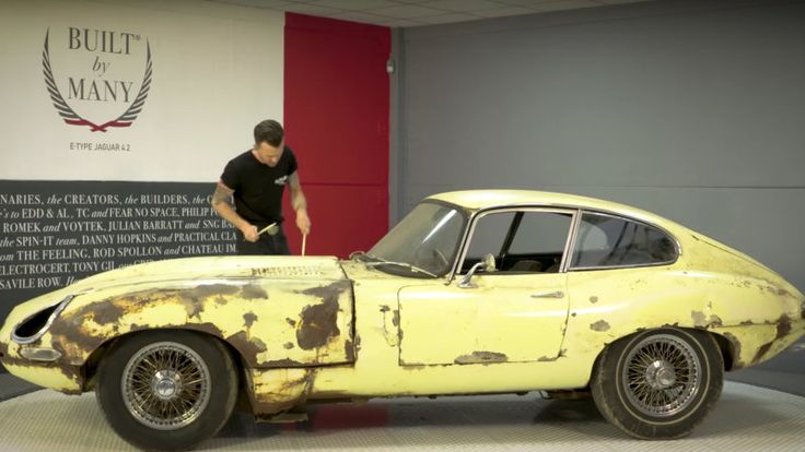 an old yellow sports car on display in a museum with a man standing next to it