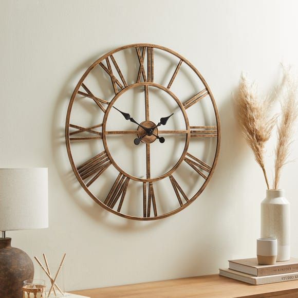 a large clock on the wall next to a table with a lamp and vases