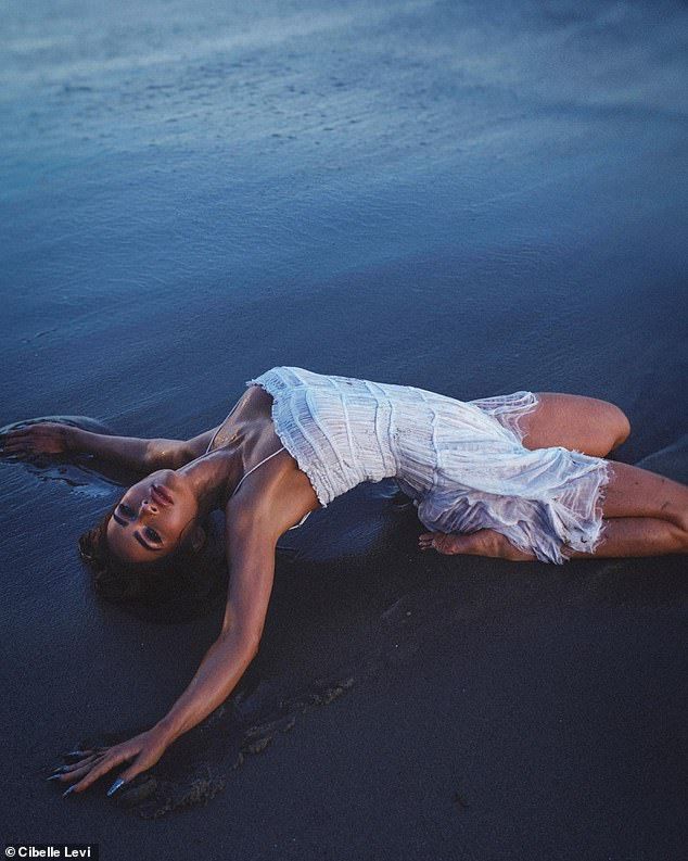 a woman laying on the beach in white dress